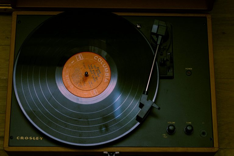 A dark wood-toned turntable sits with its tonearm resting near a black vinyl record, seen close up.