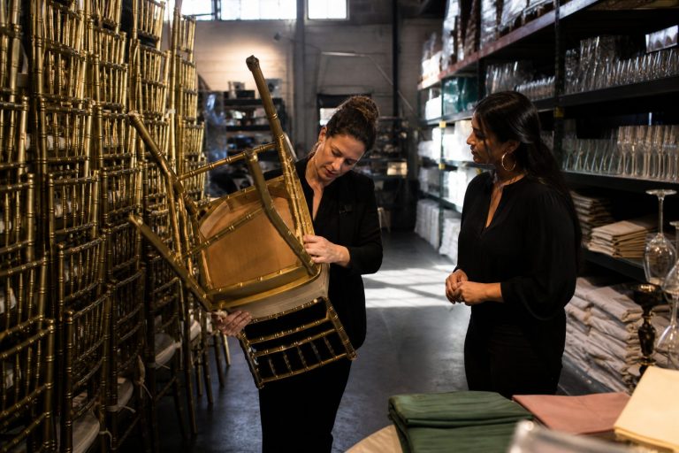 A planner turns over a gold chiavari chair to inspect it in an event rental warehouse