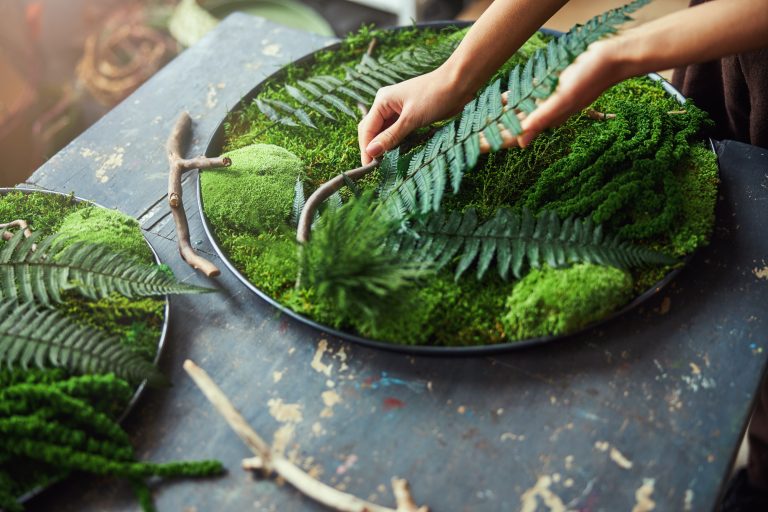Hands pressing fern into a bed of moss in a shallow tray - a workshop project a guest will carry home.